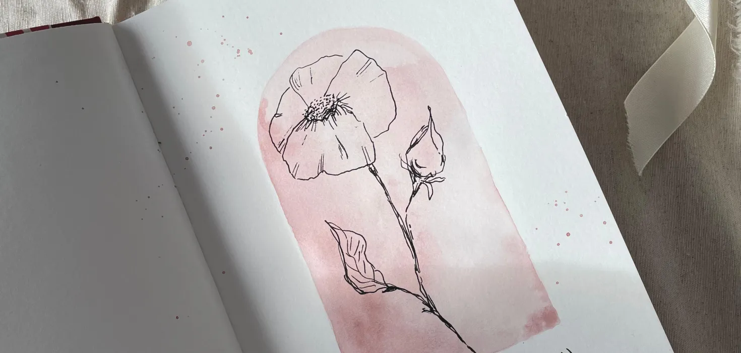 Offenes Skizzenbuch mit einer zarten Blumenzeichnung auf rosafarbenem Hintergrund, daneben Pinsel und Wasserglas