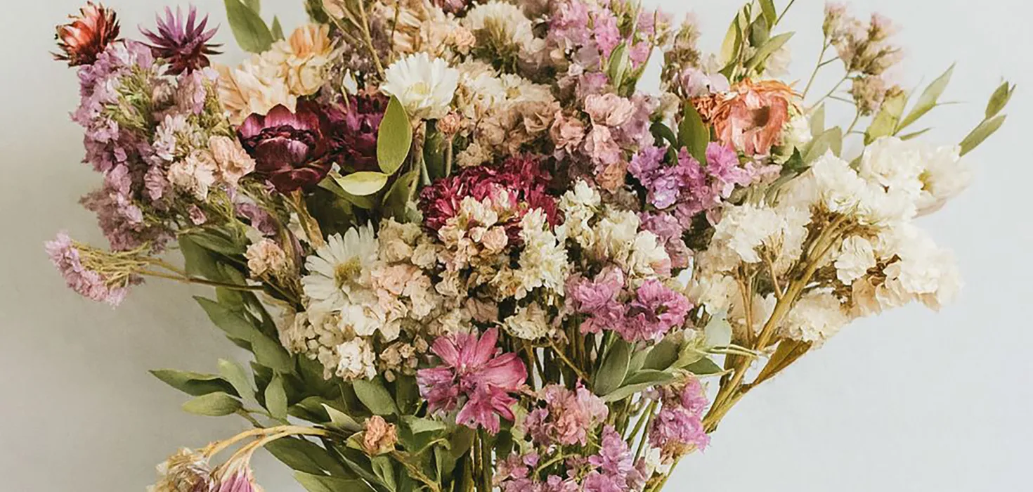 Bunter Blumenstrauß aus getrockneten Blüten in einer gestreiften Vase in warmen Gelb- und Brauntönen