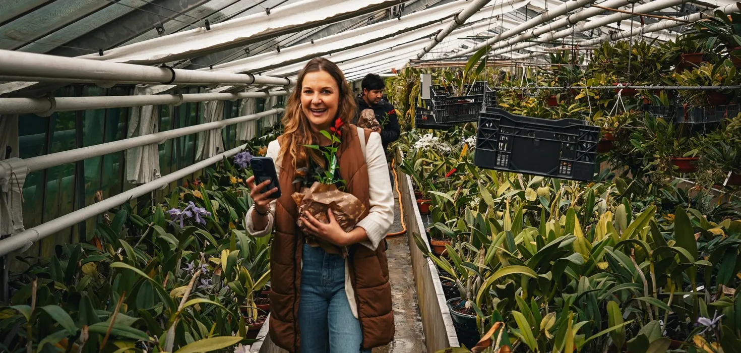 Frau mit Pflanze und Smartphone in einem Gewächshaus voller Orchideen
