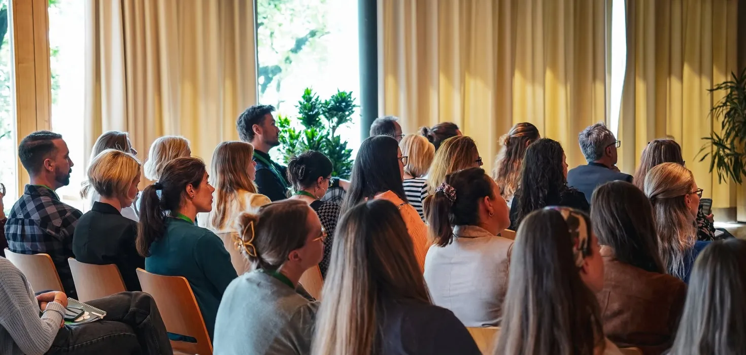 Menschen sitzen in einem hellen Veranstaltungsraum und verfolgen aufmerksam einen Vortrag oder eine Präsentation