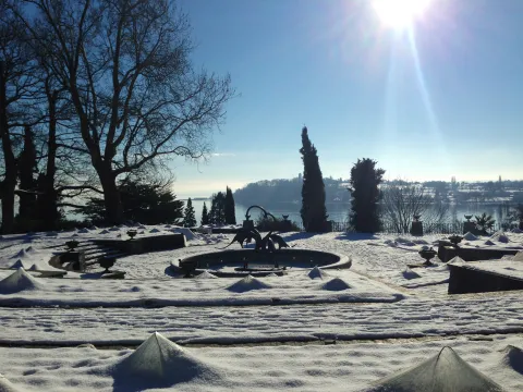 Schneebedeckte Mediterrane-Terrassen mit Brunnen und kahlen Bäumen unter klarem Himmel und Sonnenstrahlen