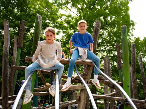 Zwei Kinder sitzen auf einer Holzstruktur mit zwei Metallrutschen im Mainau-Kinderland