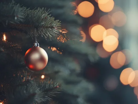 Goldene Weihnachtskugel hängt am Baum, im Hintergrund leuchten Lichter