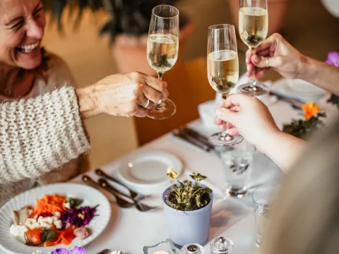 Neujahrsbrunch Drei Gläser Sekt werden in einem festlich gedeckten Tisch mit buntem Essen und Blumen in Töpfen angestoßen