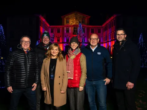 Sechs Personen stehen vor einem weihnachtlich und festlich beleuchteten Schloss