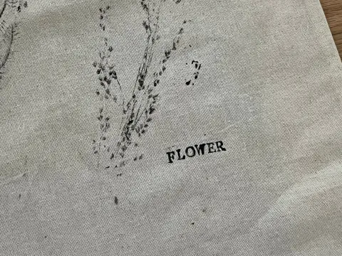 Stoff mit zartem Pflanzenabdruck in Schwarz und dem Schriftzug ‘Flower’