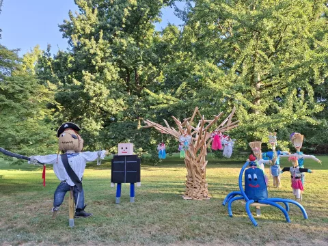 Auf einer Rasenfläche stehen mehrere fantasievoll gestaltete Vogelscheuchen und Figuren, darunter ein Pirat, ein Roboter, ein Holzbaum und eine blaue Krakenfigur. Die Szenerie gehört zur Vogelscheuchen-Ausstellung „Seegestalten“