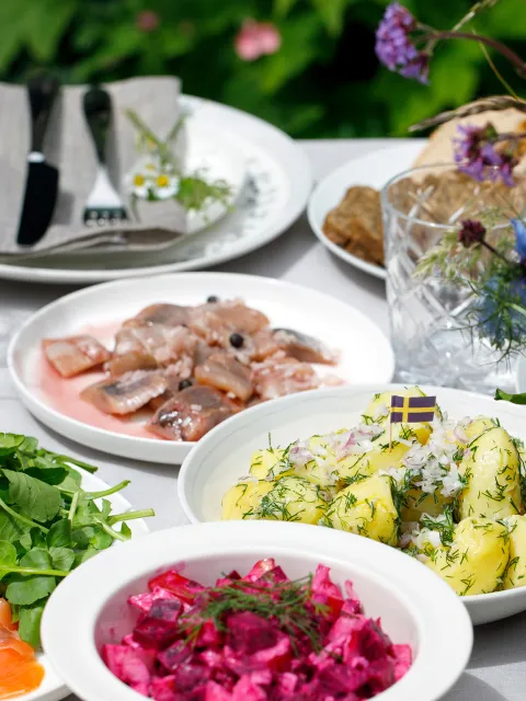 Tisch mit verschiedenen schwedischen Gerichten und einem Sommerblumenstrauß