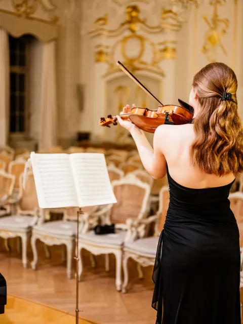 Geigerin in schwarzem Kleid spielt in einem festlich eingerichteten Saal vor einem Notenständer