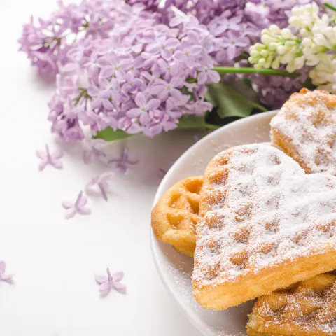 Herzförmige Waffel mit Puderzucker bestäubt und Fliederblüten