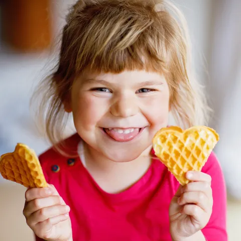 Mädchen mit zwei Waffeln in der Hand lacht in die Kamera