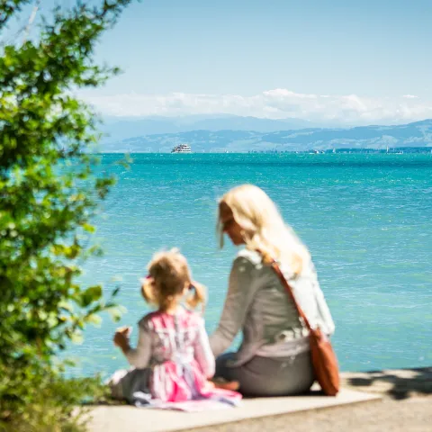 Frau mit Kind sitzt am Ufer und blickt auf den Bodensee