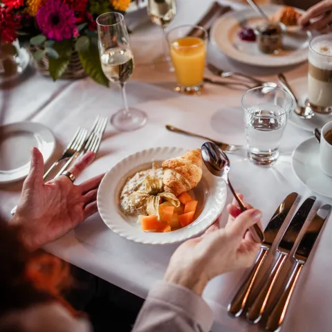 Ein gedeckter Tisch mit Herbstblumen, Sektgläsern und Orangensaft sowie einem Frühstückscroissant