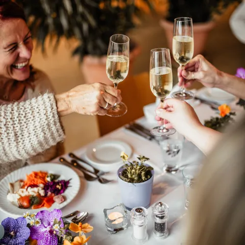 Drei Gläser Sekt werden in einem festlich gedeckten Tisch mit buntem Essen und Blumen in Töpfen angestoßen